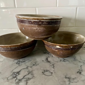 Set of 3 thrown pottery bowls, brown with ribbed design near rim in darker brown, signed on bottom, beige interiors, excellent condition.