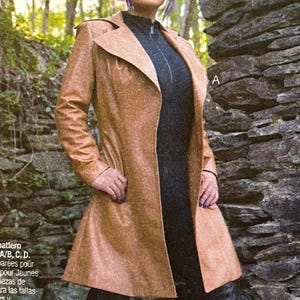 May include: A tan, long coat with a notched collar and a flared hem. The coat is worn over a dark gray top with a zipper. The background includes a stone wall and foliage. The text in the image says "Separate cup size pattern pieces for Misses': A/B, C, D."