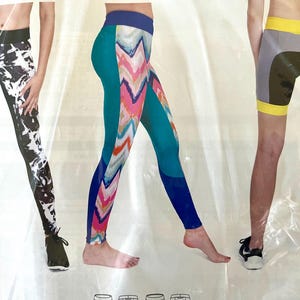 May include: Three pairs of athletic leggings and shorts are displayed. One pair of leggings is black and white, another is teal with a colorful chevron design, and the third is gray shorts with yellow trim.