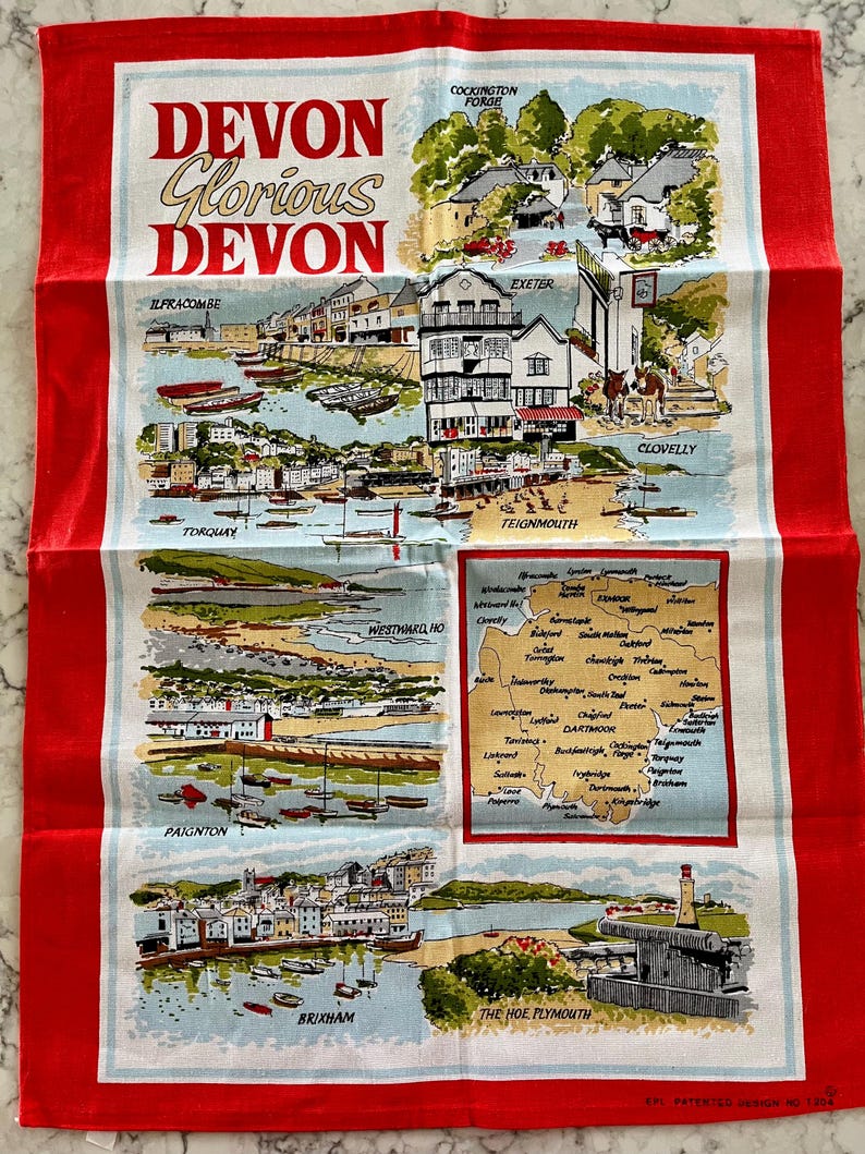 May include: A red tea towel with a white design featuring a map of Devon, England, with illustrations of various towns and cities, including Ilfracombe, Cockington Forge, Exeter, Torquay, Paignton, Brixham, Teignmouth, Westward Ho!, Clovelly, and The Hoe Plymouth. The text "Devon Glorious Devon" is printed at the top of the towel.