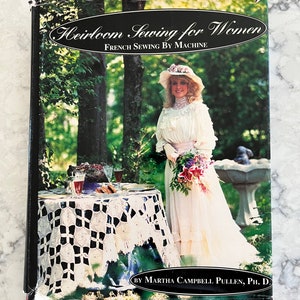 Puede incluir: Un libro titulado "Heirloom Sewing for Women: French Sewing by Machine" de Martha Campbell Pullen, Ph.D. La portada muestra a una mujer con un vestido y un sombrero blancos de pie en un jardín.