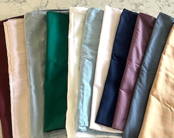 May include: A collection of eleven rectangular fabric swatches arranged side-by-side in a fan-like display. The colors include deep burgundy, pale pink, sage green, emerald green, white, light blue, cream, navy blue, mauve, slate blue, and tan.