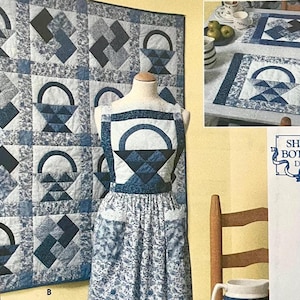 May include: A sewing pattern for a quilt, placemats, and an apron featuring blue and white basket and geometric block designs. The pattern includes the text Shirley Botsford Designs and displays finished items on a mannequin and a table setting.