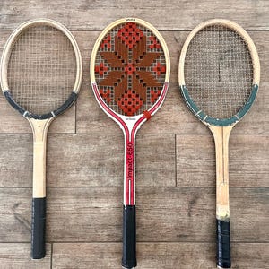 May include: Three tennis rackets arranged side by side. The left racket has a black throat and handle. The center racket features a red and white frame with the text Impact-650 and a brown and red woven star pattern. The right racket has a green throat.