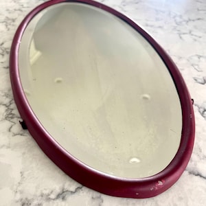 Vintage or antique wine-colored oval metal mirror with beveled reflective glass, wire hanger, great condition; 20&quot; x 10&quot; x .5&quot;.