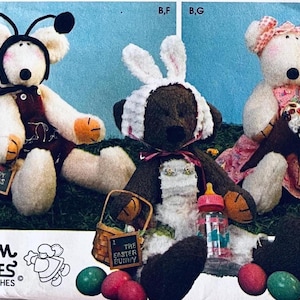 Puede incluir: Tres osos de peluche con diferentes atuendos y accesorios. Uno lleva una diadema de mariquita, otro orejas de conejo blancas y un biberón, y otro un vestido floral con un cono. Cada oso sostiene un cartel con las etiquetas Lady Bugs, The Easter Bunny o Rocky Road Ice Cream.