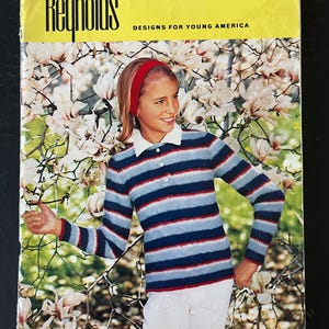 May include: Vintage "Reynolds Designs for Young America" knitting pattern book. The cover features a young person wearing a striped blue, white, and red sweater. The background includes white and pink flowers. The book's cover is yellow with black text.