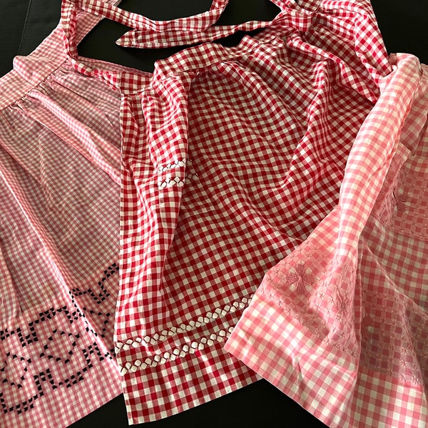 Vintage chicken scratch embroidered gingham adult-size aprons, black on pink, red & white on red, pink on pink, all charming and functional.