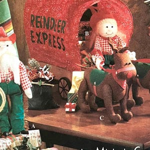 May include: A red and white plaid cowboy Santa Claus doll with a white beard and a lasso. A red and white plaid doll with blonde hair is riding a brown reindeer. The reindeer is pulling a red wagon with the words "Reindeer Express" on the side.