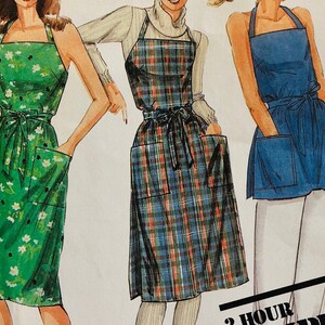 May include: Illustration of three aprons. The first is green with a white floral pattern, the second is a plaid pattern in blue, red, and black, and the third is solid blue. Each apron has a tie at the waist and pockets.
