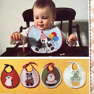 May include: Four embroidered bibs with different designs. The bibs are white with a red, green, or blue trim. The designs include a ghost, a bear, Santa Claus, and a bunny rabbit.