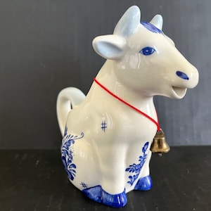 Vintage Delft ceramic blue and white cow pitcher sporting a brass bell on red thread, tail handle, excellent condition; 5.25&quot; x 5&quot; x 2.75&quot;.