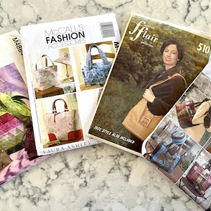 May include: Four different sewing patterns for bags. The patterns are from McCall's, Butterick, and Fashion Flair. The patterns feature various styles of bags, including totes, satchels, and bucket bags. The patterns are printed on white paper with color illustrations.
