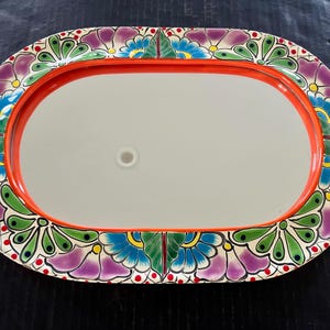 May include: Oval decorative tray with a red rim and a floral design. The tray's border features a colorful pattern of purple, blue, and green flowers. The center of the tray is a light gray color.