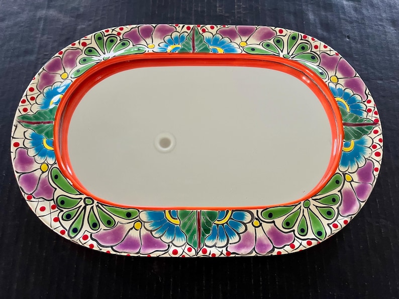 May include: Oval decorative tray with a red rim and a floral design. The tray's border features a colorful pattern of purple, blue, and green flowers. The center of the tray is a light gray color.