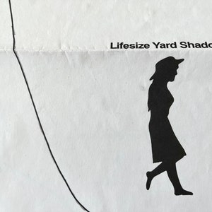 Könnte beinhalten: Eine schwarz-weiße Silhouette einer Person, die geht, mit dem Text "Lifesize Yard Shadow" über der Silhouette.