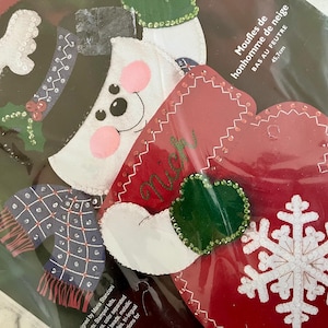 Op de afbeelding: Een vilt sneeuwpop knutselset met rode wanten, een groene want en een sneeuwvlok ontwerp. De set bevat instructies voor het maken van een sneeuwpop, wanten en een sneeuwvlok. De set is 45,7 cm hoog.