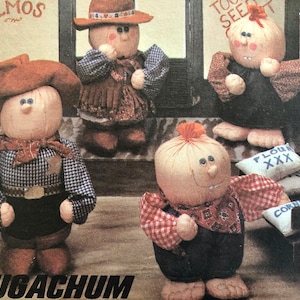 Może przedstawiać: Cztery ręcznie robione lalki z tkaniny ubrane w kowbojskie stroje. Lalki stoją na drewnianej podłodze z brązowym i białym wzorzystym dywanem. Lalki mają na sobie kapelusze, koszule i spodnie. Lalki się uśmiechają i mają duże oczy. Lalki są wykonane z tkaniny i mają rustykalny, ręcznie robiony wygląd.