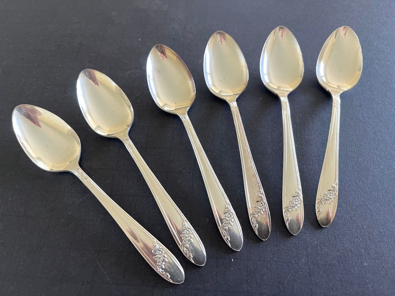 Set of 6 silverplate demitasse spoons by Oneida, shiny silver with spray of roses on bottom handle; each 4.5" long. Selling as a set of 6.