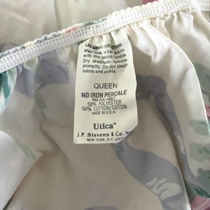 May include: Close-up of a floral patterned Queen size bed sheet. The sheet features a white background with pink, blue, and green floral designs. A tag with washing instructions and the brand "Utica" is visible.