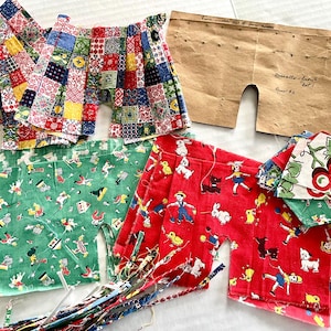 Puede incluir: Una colección de shorts de tela vintage en varios patrones y colores. Algunos shorts son de patchwork, mientras que otros presentan estampados lúdicos de niños, animales y cerezas. También se incluye un patrón de papel marrón.