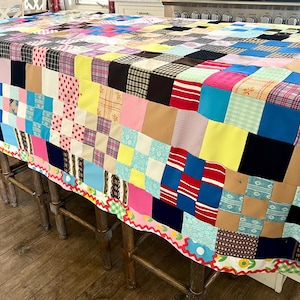 Peut inclure: Une courtepointe patchwork colorée recouvrant une table. La courtepointe présente des carrés de tissu variés dans des tons de bleu, rose, jaune et marron. Les bords sont ornés d'une bordure festonnée. Article fait à la main.