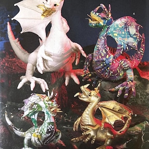 May include: Four dragon figurines in different colours. One is white with gold accents, another is multicoloured with purple, blue, and pink, a third is gold with red, and the last is green and white. All have wings and are posed on a rocky surface.