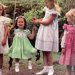 Peut inclure: Plusieurs jeunes filles vêtues de robes vintage sont réunies à l'extérieur. L'une d'elles est sur une balançoire. Les robes sont blanches, vertes et roses, avec des détails comme des broderies, des manches bouffantes et des cols Claudine. La scène évoque l'enfance et le jeu.
