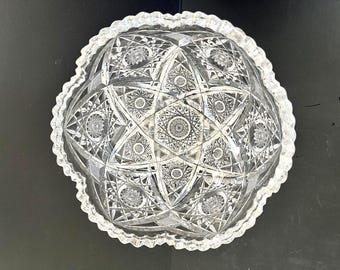 Könnte beinhalten: Eine klare, runde Glasschale mit einem komplizierten, facettierten Sternmuster, das in die Oberfläche geschliffen ist. Die Schale hat einen gewellten, gezackten Rand und ein tiefes, konkaves Inneres, das komplexe geometrische Designs zeigt.