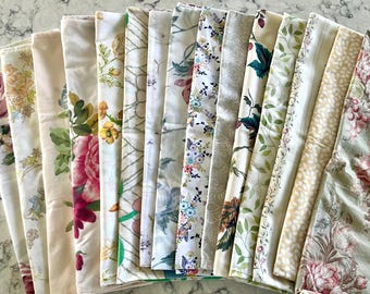 May include: A collection of folded fabric swatches featuring various floral, botanical, and geometric patterns in shades of cream, pink, green, blue, and yellow. The textiles display diverse prints including roses, vines, leaves, and intricate line work.