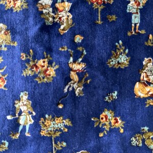 May include: Close-up of a blue fabric with a repeating pattern of figures and floral elements in shades of gold, orange, and green. The design features small human figures and stylized flowers.