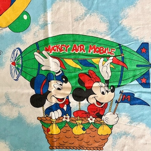 May include: A vintage fabric featuring Mickey and Minnie Mouse in a hot air balloon labeled "Mickey Air Mobile." The design includes Donald Duck with balloons, a green airship, and a blue sky background.