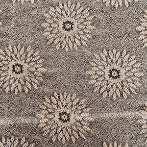 May include: Close-up of a textured fabric featuring a repeating floral pattern. The flowers are beige with a dark brown centre, set against a dark brown background. The design creates a vintage or retro aesthetic.