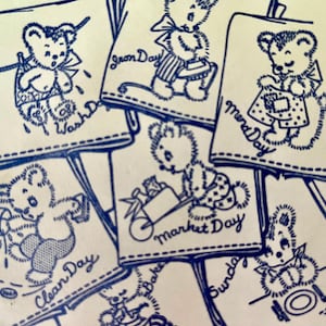 Könnte beinhalten: Eine Sammlung von blau-weißen Illustrationen im Vintage-Stil, die Teddybären bei verschiedenen Hausarbeiten zeigen. Jeder Bär ist auf einem rechteckigen Banner abgebildet, mit Texten wie "Wash Day" und "Market Day".