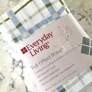 May include: A white full fitted sheet with a plaid pattern in light blue and olive green. The packaging features the text Everyday Living, Full Fitted Sheet, 200 Thread Count, Machine Washable, All Around Elastic For A Better Fit, 54 in x 75 in.
