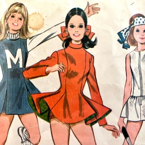 Könnte beinhalten: Eine Vintage-Schnittmuster-Illustration mit drei Figuren in Sportkleidung. Eine trägt ein blaues ärmelloses Kleid mit einem weißen M und hält ein Megafon. Eine andere trägt ein langärmeliges orangefarbenes Kleid. Die dritte trägt ein weißes ärmelloses Kleid.