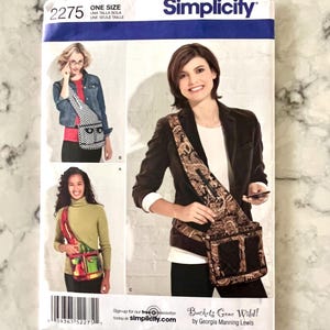 May include: Simplicity sewing pattern 2275 for a crossbody bag, featuring multiple views. The pattern cover displays images of the finished bags in various fabrics and styles. The text "Buckets Gone Wild!" is also visible.
