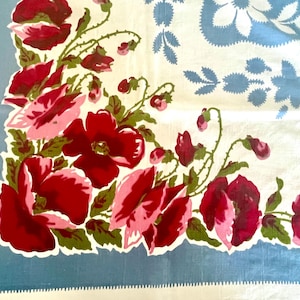 May include: A square textile featuring a corner cluster of vibrant red and pink poppy flowers with green leaves. The fabric has a light blue border and a secondary light blue floral pattern printed on a white background with a serrated edge finish.
