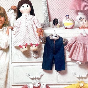 May include: A young girl stands next to a white dresser adorned with children's clothing and accessories. A doll in a pink dress and bunny slippers sits on the dresser. Other items include a blue jumpsuit, a pink dress, and decorative figurines.