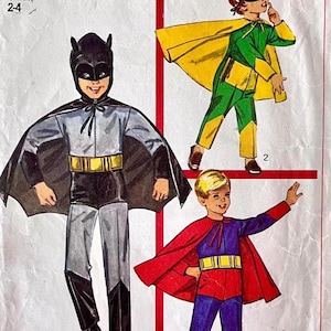 May include: Vintage sewing pattern featuring illustrations of children's superhero costumes. The costumes include a Batman-inspired outfit with a bat cowl and cape, and two other superhero designs with capes and belts. The pattern is for sizes 2-4.