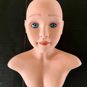 May include: A bald, porcelain mannequin head with a bust, featuring painted blue eyes and a neutral expression.