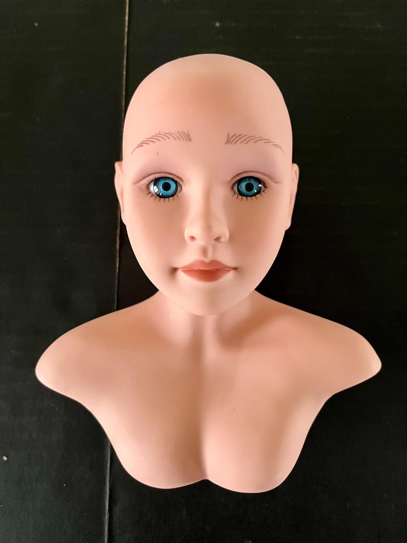 May include: A bald, porcelain mannequin head with a bust, featuring painted blue eyes and a neutral expression.