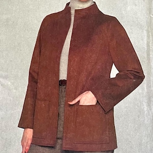 Puede incluir: Una chaqueta de ante marrón con cuello alto y corte largo y holgado. La chaqueta tiene cierre de cremallera y dos bolsillos.