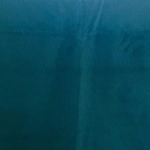 Puede incluir: Primer plano de una tela de color verde azulado con textura acanalada vertical. La tela tiene un ligero brillo y una sutil variación de color, creando profundidad. El material parece ser de color sólido, sin patrones ni diseños visibles.