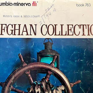 May include: A vintage book cover for a Russi's Yarn & Needlecraft Afghan Collection. The cover features a blue and white nautical scene with a ship's wheel and a lantern. The book is titled "Afghan Collection" and the price is $2.50.