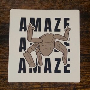 May include: A white square sticker with the word "AMAZE" in black block letters, repeated three times. A stylized brown insect-like creature is centered on the sticker. The creature has six legs and a segmented body.