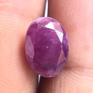 Peut inclure: Une pierre précieuse à facettes de forme ovale d'une couleur magenta-rose profond. La pierre présente une surface polie avec de multiples facettes triangulaires qui reflètent la lumière, mettant en valeur une qualité translucide et une teinte vive.