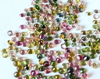 Puede incluir: Una gran colección de piedras preciosas redondas y facetadas en varios tonos de verde, rosa y amarillo. Las piedras preciosas están esparcidas sobre una superficie blanca.