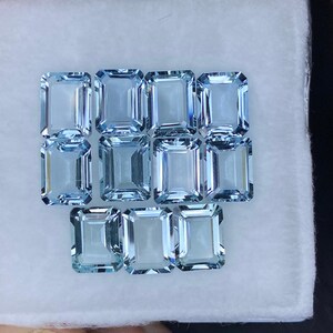 Puede incluir: Una colecci&oacute;n de 12 piedras preciosas de aguamarina azul claro, talladas en forma de esmeralda. Las piedras preciosas est&aacute;n dispuestas en tres filas de cuatro, con la fila inferior ligeramente desplazada.