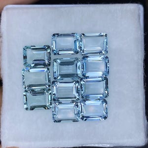 Puede incluir: Una colecci&oacute;n de 12 piedras preciosas de aguamarina azul claro en talla esmeralda rectangular. Las piedras preciosas est&aacute;n dispuestas en una caja con forro blanco.